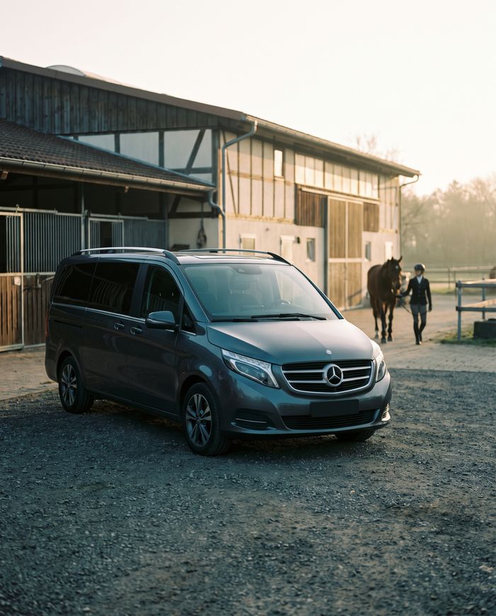 Dunkelgrauer Kastenwagen vor einer Reitanlage im Abendlicht.